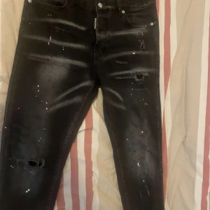 Svarta slim jeans med slitningar - Säljer ett par svarta skinny jeans med coola slitningar och färgstänk. Jeansen har en tight passform och klassisk femficksdesign. Perfekta för dig som gillar en edgy streetstil. Priset kan diskuteras.