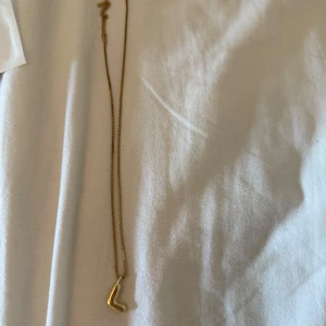 Guldigt halsband med L-berlock - Snyggt halsband i guldton med en enkel och stilren L-formad berlock. 