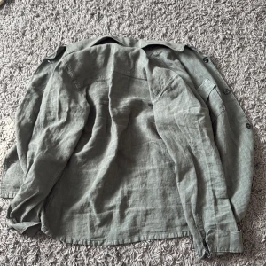 Grön overshirt i linne - Snygg grön overshirt från dressman med klassisk krage och två bröstfickor med knappar. Skjortan har långa ärmar och är tillverkad i ett luftigt linnematerial, perfekt för lager-på-lager. Enkel och stilren design som passar till det mesta. 