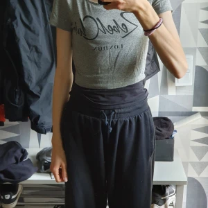 Grå croppad topp med tryck - Säljer en grå croppad topp med svart texttryck framtill. T-shirten har korta ärmar och rund halsringning, perfekt för en avslappnad och trendig look. Enkel att matcha med både jeans och mjukisbyxor.