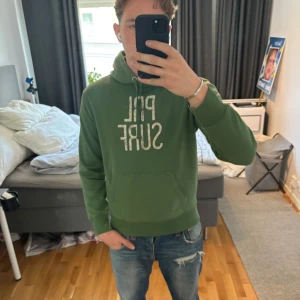 Grön hoodie från Polo Ralph Lauren - Snygg grön hoodie från Polo Ralph Lauren med vit PRL SURF-tryck på bröstet. Klassisk känguruficka, snörning i huvan och mjukt bomullsmaterial. Perfekt för en chill och avslappnad stil. Storlek S men passar M. Jag är 185cm.