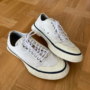 Vita sneakers från Eytys strl 40 - Snygga vita sneakers från Eytys i textil med robust gummisula och vita snören. Klassisk låg modell med lila detalj baktill och mörkblå rand längs sulan. Lite smutsiga och veckiga, lite nötta vid hälen (se bild). Annars riktigt sköna och i bra skick! Finns i Linköping eller skickas.   Kolla gärna in mina andra annonser,   Allt gott,  K