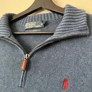 Blå half zip tröja Polo Ralph Lauren - Snygg blå stickad tröja från Polo Ralph Lauren i 100% bomull. Tröjan har en ribbad krage, half zip-dragkedja med läderdetalj och det klassiska röda broderade logot på bröstet. Perfekt för lager-på-lager och chill stil. Endast använd en gång, perfekt skick till ett mycket bra pris!
