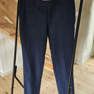 Mörkblå linnebyxor med rak passform - Snygga mörkblå kostymbyxor med klassisk rak passform och bälteshällor. Byxorna har diskreta bakfickor och stängs med dold dragkedja fram. Perfekta för en clean och stilren look, särskilt under varmare dagar.
