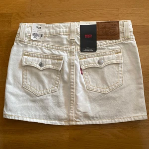 Vit jeanskjol från Levi’s  - Vit jeanskjol från Levi's i klassisk minilängd. Kjolen har snygga bakfickor med lock och knappar. Den är helt perfekt nu till sommaren😊Kjolen är aldrig använd, helt ny med lappar kvar! Kjolen finns inte längre att köpa heller. Skriv gärna ifall du har frågor!💗