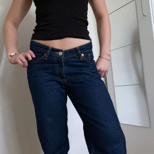 Mörkblå midwaist jeans från Zara - Säljer ett par mörkblå jeansbyxor från Zara med raka ben. Byxorna har kontrastsömmar i gult och normal passform. Perfekta för en stilren och enkel look. Det är inte stretchiga och är något högre i ryggen en där fram. 