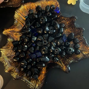 Svarta och blå pärlor i glas - Ett mixat set med svarta och några mörkblå pärlor i olika former och storlekar, perfekta för att skapa egna smycken som armband, halsband eller örhängen. Pärlorna är tillverkade i glas och har både runda, kantiga och blommiga former.