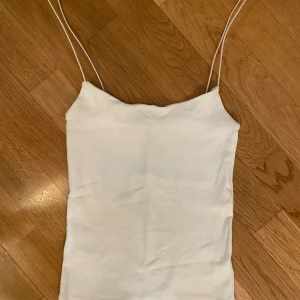 Vit enkel linnetopp med smala band - Säljer en stilren vit linnetopp med tunna axelband. Toppen har en rak, minimalistisk design och är perfekt för varma dagar. Materialet känns mjukt och lätt mot huden. Passar snyggt till både jeans och kjol.