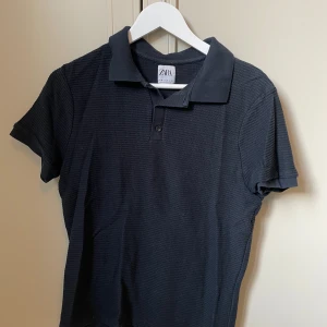 Svart pikétröja från Zara - Säljer en stilren svart pikétröja från Zara. Tröjan har korta ärmar och en klassisk krage med knappar. Perfekt för en avslappnad men ändå snygg look.