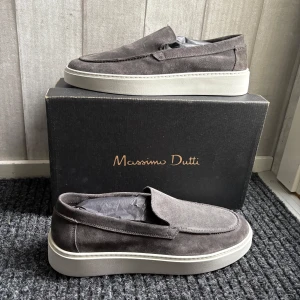 Gråa mockaloafers från Massimo Dutti - Snygga gråa loafers i mocka från Massimo Dutti. Skorna har en stilren design med en vit sula som ger en modern touch. Perfekta för en avslappnad men ändå elegant look. Aldrig använda endast testade, köpta i Göteborg och var för stora