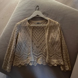 Beige spetskofta från JDY - Säljer en elegant beige spetskofta från JDY. Koftan har ett vackert spetsmönster och trekvartsärmar.