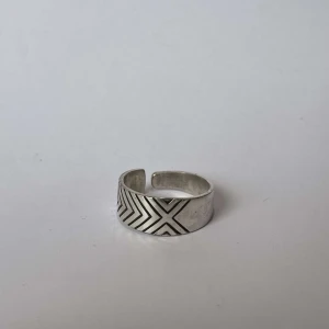 Silverfärgad ring med geometriskt mönster - Stilren och modern ring i silverfärg med ett snyggt geometriskt mönster. Ringen har en öppen design vilket gör den justerbar för olika storlekar. Perfekt för att ge en minimalistisk touch till din stil.