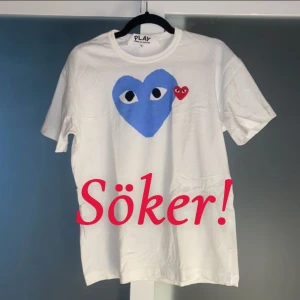 Vit t-shirt med blått hjärta från Play - Söker en vit t-shirt från Play med ett stort blått hjärta och ett litet rött hjärta med ögon på bröstet. T-shirten har en klassisk rund hals och korta ärmar. Perfekt för en avslappnad stil. I strl m eller s