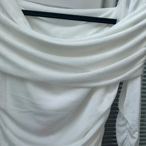 Vit klänning från Gina Tricot - Säljer en elegant vit klänning från Gina Tricot. Klänningen har en draperad design med långa ärmar och är tillverkad i ett mjukt material. Perfekt för en stilren look☺️! Det är ett tjockt material så inte see-through.