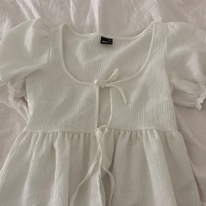 Vit topp från Gina Tricot - Säljer en söt vit topp från Gina Tricot med puffärmar och knytning framtill. Aldrig använd!