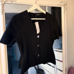 Svart blus från Gina Tricot - Snygg svart blus/tshirt från Gina Tricot med korta ärmar och v-ringning. Aldrig använd så är i nyskick med prislappen kvar 🥰