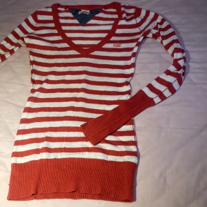 Röd- och vitrandig tröja från Tomy Hilfiger Denim - Säljer en röd- och vitrandig tröja från Hilfiger Denim. Tröjan har en v-ringad hals och långa ärmar med ribbade muddar. 