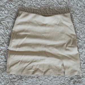 Beige kjol från Gina Tricot - Beige kjol från Gina Tricot i en kort modell. Kjolen har en liten slits framtill. 