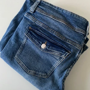 Blå jeans från Ginatricot  - Snygga blå jeans från Ginatricot med klassisk femficksdesign och dubbla knappar i midjan. Perfekta för en avslappnad stil. De har en dragkedja och bälteshällor för extra funktionalitet.