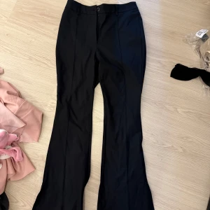 Svarta kostymbyxor med slits - Snygga svarta kostymbyxor med slits vid bensluten. Byxorna har en  bootcut-stil och kortare modell. Endast testade 