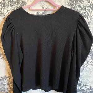 Svart ribbad tröja från Zara - Säljer en stilren svart ribbad tröja från Zara. Tröjan har långa ärmar med puffiga axlar som ger en trendig look. Aldrig använt.