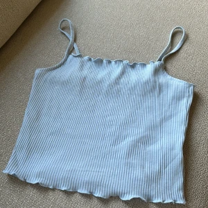 Ljusblå ribbad linnetopp från NA-KD - Säljer en ljusblå ribbad linnetopp från NA-KD. Toppen har smala axelband och en vågig kant vid halsringningen och nederkanten. Perfekt för varma dagar eller som ett lager under en jacka.