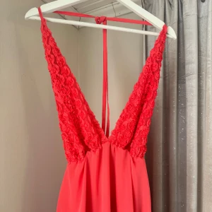 Röd långklänning med spetsdetaljer - Snygg röd långklänning med spetsdetaljer på axelbanden och öppen rygg. Perfekt för sommarens fester eller som balklänning. Klänningen har en v-ringad design och knytband i ryggen.