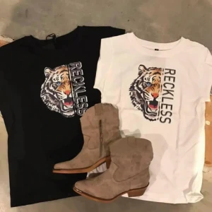 Svart och vit t-shirt med tigertryck från Prepair - Snygga t-shirts från Prepair i svart och vitt med ett coolt tigertryck och texten 'Reckless'. Perfekt för en avslappnad stil. T-shirtsen är kortärmade och gjorda i bomull för en skön känsla.vit storlek M och L svart storlek xs. 300kr per st , du väljer färg och storlek.