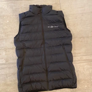 Svart dunväst från Sail Racing - Storlek 176 Det är 65cm från axeln till botten/midjan av västen Inga defekter Knappt använd