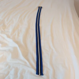 Blått randigt bälte - Snyggt blått Polo Ralph Lauren bälte med randigt mönster i svart och vitt. Perfekt för att ge en färgklick till din outfit. Bältet har en enkel design med en metallspänne som ger en stilren look.