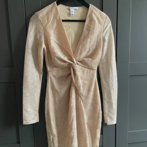Champagnefärgad glittrig klänning - Champagnefärgad klänning från NLY Trend i glittrigt material och storlek XS. Den har en lite djupare v-ringad urringning. 