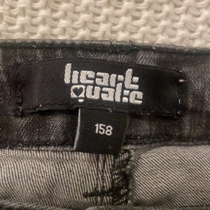 Svart kortkjol från Heartquake - Lågmidjad snygg svart kortkjol från Heartquake med slitna detaljer och knappstängning fram. Kjolen har fickor både fram och bak. Kom de prisförslag.