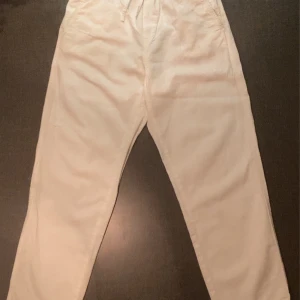 Vita linnebyxor från H&M - Säljer ett par vita linnebyxor från H&M i storlek EUR 152. Byxorna har en elastisk midja och är tillverkade i ett lätt och bekvämt material, perfekt för sommaren.