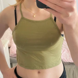 Olivgrön croppad linnetopp från H&M Divided - Säljer en olivgrön croppad linnetopp från H&M Divided. Toppen har smala axelband och en enkel design som passar perfekt för varma dagar. Perfekt för en avslappnad stil. 🌿