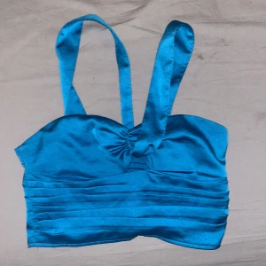 Blå satin korsett från Gina Tricot - Snygg blå korsett i satin från Gina Tricot med breda axelband och rynkdetaljer framtill. Perfekt för en stilren look. Den har en elastisk rygg för bättre passform.