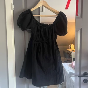 Svart klänning  - Snygg svart klänning från Cotton On med puffiga kortärmar och en smickrande off-shoulder design. Perfekt för en stilren look. Klänningen har en elastisk överdel som ger en bekväm passform.