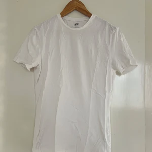 Vit t-shirt från H&M - Säljer en klassisk vit t-shirt från H&M i slim fit. Passar till alla tillfällen. Liten fläck syns på bild 3, annars helt vit.