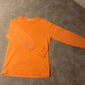 Orange långärmad tröja från Stone Island - Snygg orange långärmad tröja från Stone Island Junior. Tröjan har en rund halsringning och ett subtilt broderat logotypmärke på bröstet. Perfekt för en färgglad och stilren look. 