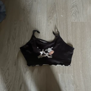 Svart croppad linnetopp med ko-tryck - Säljer en svart croppad linnetopp med smala axelband och ett gulligt ko-tryck framtill. Toppen har vågig kant nertill och är perfekt för sommaren.