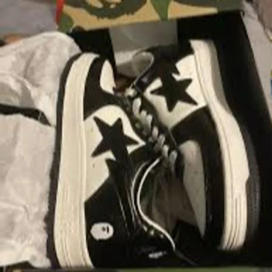 Svarta och vita BAPE sneakers - Säljer ett par klassiska BAPE sneakers i svart och vitt med den ikoniska stjärndetaljen på sidan. Skorna har snörning, rund tå och platt sula. Perfekta för dig som gillar streetwear och vill sticka ut med en unik stil.