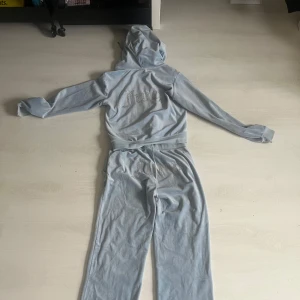 Ljusblå mjukis dress från Juicy Couture - Ljusblå mjukisbyxor från Juicy Couture med glittrig Juicy-text på baksidan. Byxorna i Stlk S men är uppsydda ca 4 cm, tröjan i stlk M 