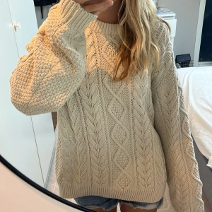 Beige stickad tröja från Vailent - Säljer en chunky beige stickad tröja från Vailent med flätstickat mönster och breda muddar. Tröjan har en oversized passform och långa ärmar, perfekt för kyliga dagar.