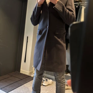 Mörkgrå rock från Hugo Boss - Säljer en stilren mörkgrå rock från Hugo Boss. Klassisk design med knäppning framtill, två fickor med lock och slits bak. Perfekt för dig som vill ha en tidlös och snygg jacka till höst och vinter. Orginalpriset är 10.000kr. skriv för mer info
