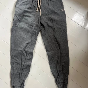 Grå mjukisbyxor från Carin Wester - Grå mjukisbyxor från Carin Wester med broderad CW-logga på benet. Byxorna har resår i midjan med snörning och muddar vid bensluten. Perfekta för en avslappnad stil och riktigt sköna att ha på sig. Knappt använda. Skicka för fler bilder💞