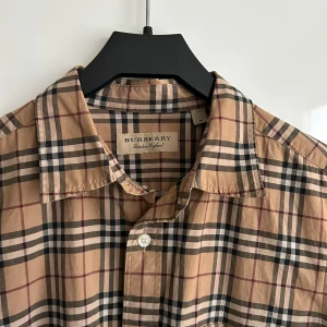 Beige rutig skjorta från Burberry - Klassisk beige rutig skjorta från Burberry. Skjortan har lång ärm, knappar framtill 