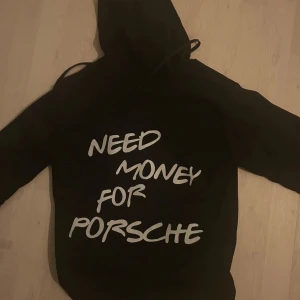 Svart hoodie med text - Säljer en svart hoodie med texten 'Need Money for Porsche' i vitt. Den har en klassisk design med huva och en stor ficka framtill. Perfekt för en avslappnad stil.