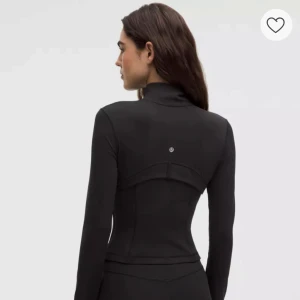 Svart träningsjacka från Lululemon - Snygg svart träningsjacka från Lululemon med figurnära passform. Jackan har dragkedja framtill, långa ärmar med tumhål och diskret logga på ryggen. Perfekt för träning eller som ett sportigt lager.