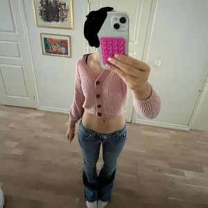 Rosa ribbad kofta - Säljer en söt rosa ribbad kofta med knappar framtill. Koftan har långa ärmar och en v-ringad design, perfekt för att hålla sig varm och stilren. Passar bra till både jeans och kjol. 
