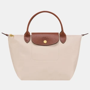Beige handväska från Longchamp - Stilren beige handväska från Longchamp med bruna handtag och lock i skinn. Väskan har guldfärgad knapp och dragkedja upptill. Perfekt storlek för vardagens alla prylar och enkel att bära i handen.