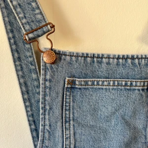 Ljusblå denim hängselbyxor - Säljer ett par klassiska ljusblå hängselbyxor i jeansmaterial med bröstficka och justerbara axelband. 